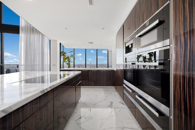 18555 Collins Ave Unit 4603, Sunny Isles Beach, FL 33160 - kitchen featuring modern cabinets, dark brown cabinets, stainless steel double oven, light stone countertops, and light marble finish flooring