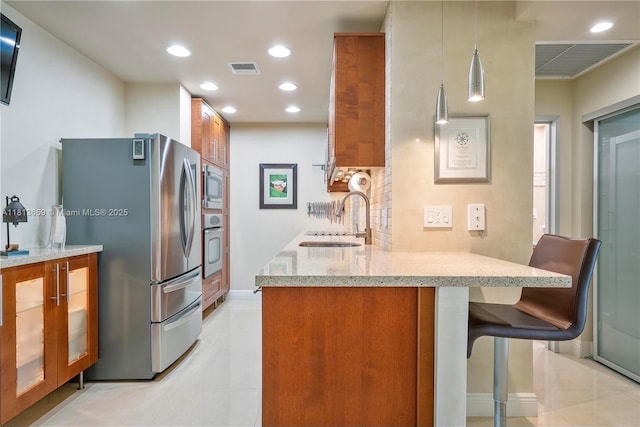 300 Bayview Dr Unit 102, Sunny Isles Beach, FL 33160 - kitchen featuring brown cabinets, appliances with stainless steel finishes, a sink, light stone counters, and a breakfast bar