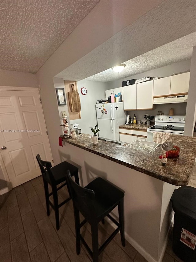 3995 W Mcnab Rd Unit B212, Pompano Beach, FL 33069 - kitchen featuring white appliances, under cabinet range hood, a peninsula, a breakfast bar area, and a textured ceiling