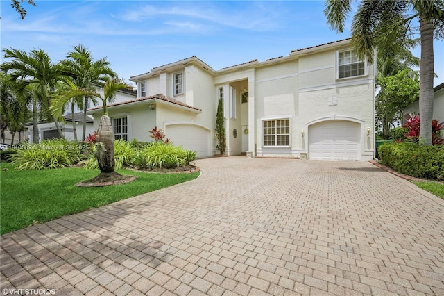 view of front of house featuring an attached garage, decorative driveway, stucco siding, and a front yard