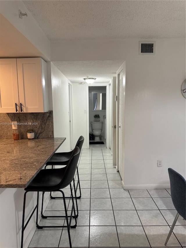 10661 SW 108th Ave Unit 2E, Miami, FL 33176 - kitchen with a textured ceiling, light tile patterned floors, a kitchen bar, backsplash, and white cabinets
