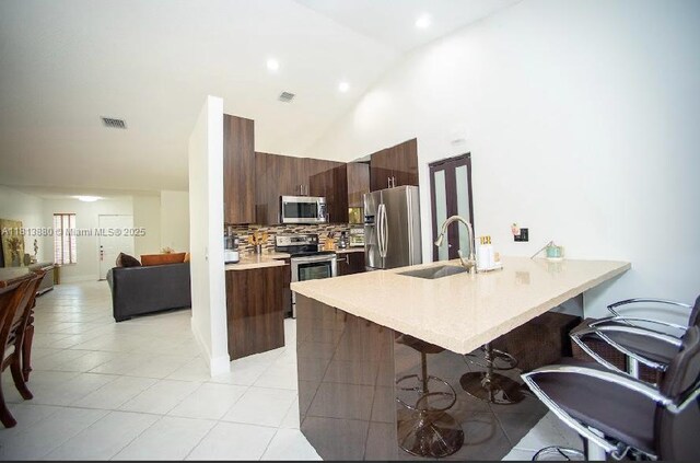 1353 Majesty Ter, Weston, FL 33327 - kitchen with appliances with stainless steel finishes, a kitchen bar, light countertops, a peninsula, and high vaulted ceiling