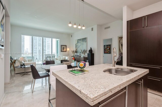 900 Brickell Key Blvd Unit 1702, Miami, FL 33131 - kitchen with a sink, a kitchen island with sink, hanging light fixtures, dark brown cabinetry, and open floor plan
