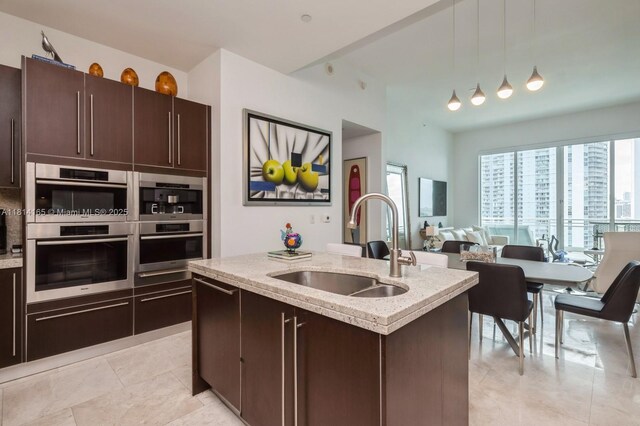 900 Brickell Key Blvd Unit 1702, Miami, FL 33131 - kitchen with a sink, stainless steel double oven, dark brown cabinetry, a kitchen island with sink, and hanging light fixtures