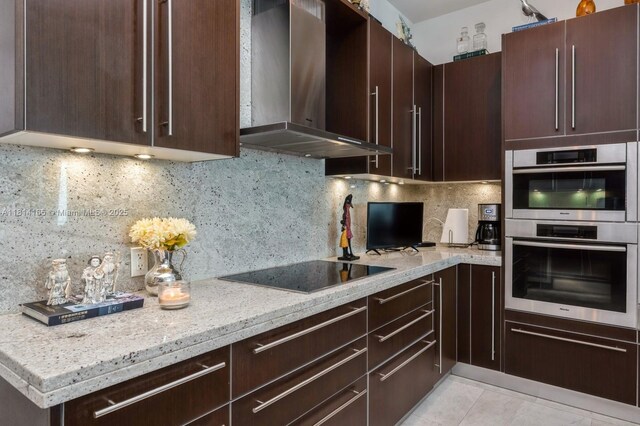 900 Brickell Key Blvd Unit 1702, Miami, FL 33131 - kitchen with wall chimney range hood, stainless steel double oven, black electric cooktop, backsplash, and dark brown cabinetry