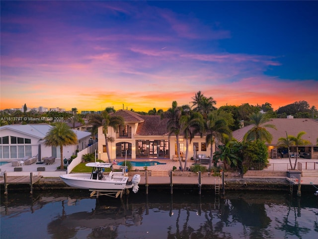 1437 SE 13th St, Deerfield Beach, FL 33441 - back of property at dusk with a patio area, an outdoor pool, a tile roof, a water view, and stucco siding