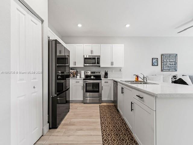 18058 SW 147th Ct, Miami, FL 33187 - kitchen with stainless steel appliances, white cabinets, light countertops, light wood finished floors, and a peninsula