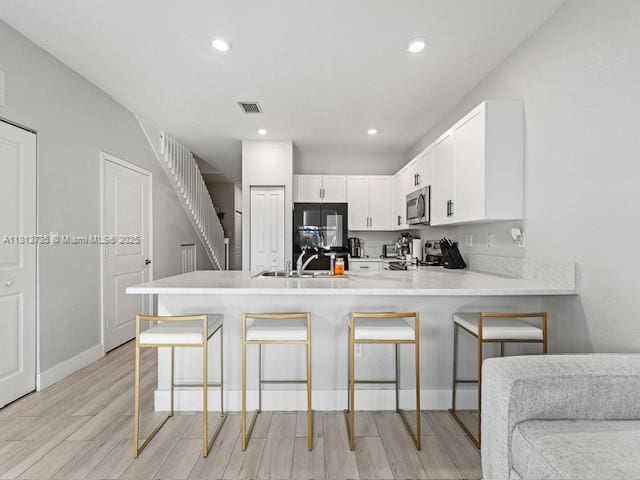 18058 SW 147th Ct, Miami, FL 33187 - kitchen with stainless steel microwave, a peninsula, light wood finished floors, light countertops, and white cabinetry