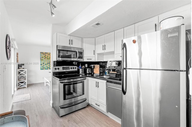 1370 NE 40th Dr, Oakland Park, FL 33334 - kitchen featuring appliances with stainless steel finishes, white cabinetry, light wood-style floors, and dark countertops
