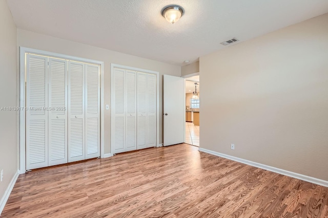 9802 N Military Trl, Palm Beach Gardens, FL 33410 - unfurnished bedroom with multiple closets, light wood finished floors, baseboards, and a chandelier