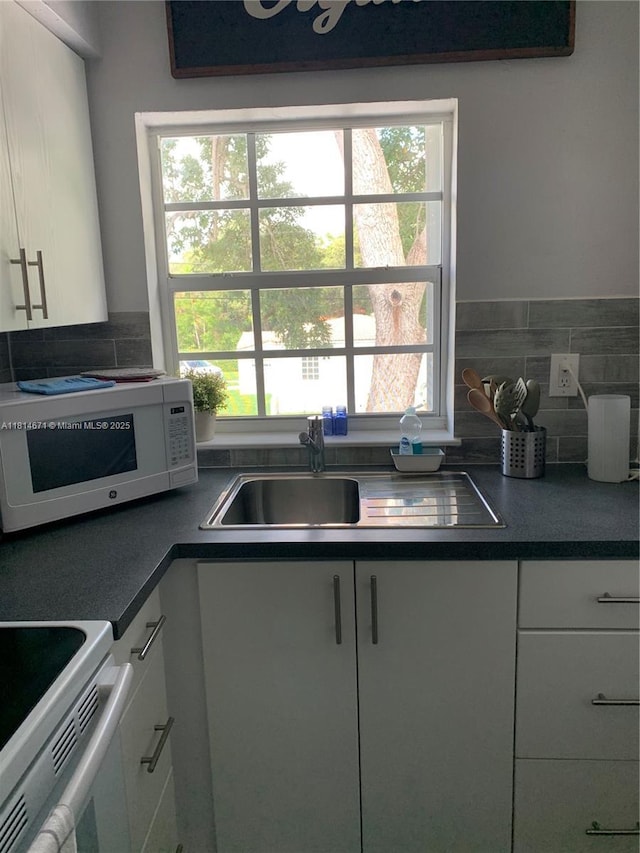 1105 NE 119th St, Biscayne Park, FL 33161 - kitchen with white appliances, healthy amount of natural light, white cabinets, and dark countertops