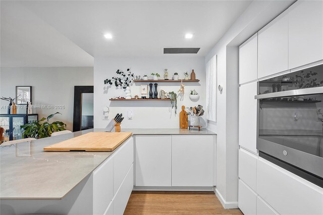 2150 Sans Souci Blvd Unit B311, North Miami, FL 33181 - kitchen with open shelves, oven, light countertops, white cabinets, and light wood finished floors