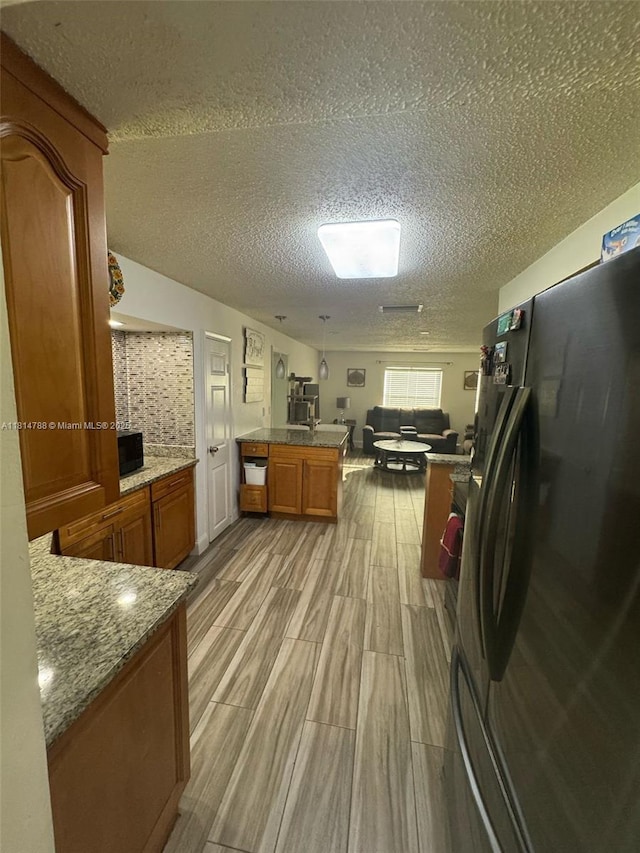 4706 25th Ave SW, Naples, FL 34116 - kitchen with freestanding refrigerator, brown cabinetry, a textured ceiling, light wood-type flooring, and open floor plan