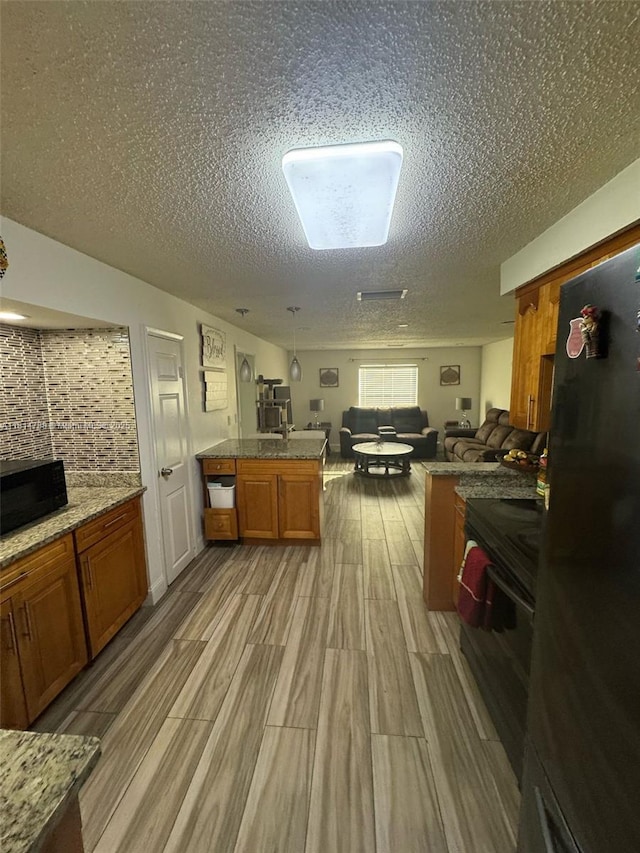 4706 25th Ave SW, Naples, FL 34116 - kitchen with black appliances, brown cabinetry, open floor plan, a textured ceiling, and light wood-style flooring