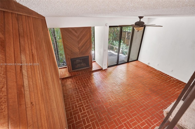2591 Trapp Ave Unit 4, Miami, FL 33133 - unfurnished living room featuring brick patterned floors, a textured ceiling, a glass covered fireplace, ceiling fan, and baseboards