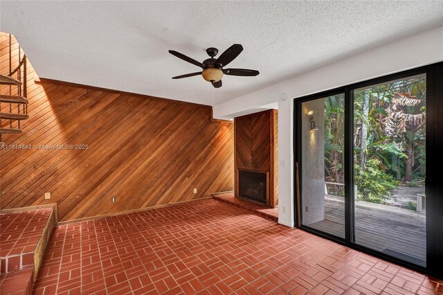 2591 Trapp Ave Unit 4, Miami, FL 33133 - unfurnished living room with wooden walls, a fireplace, ceiling fan, stairway, and a textured ceiling