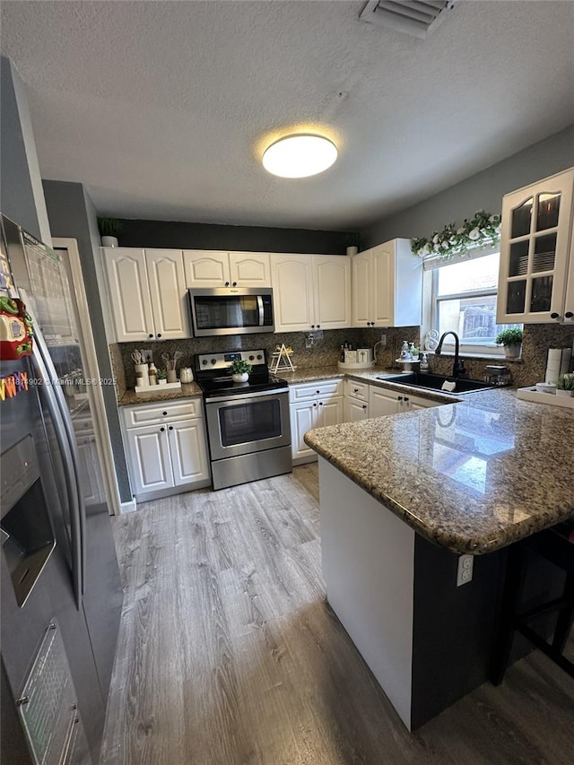 238 Magnolia Ave, Davie, FL 33325 - kitchen with appliances with stainless steel finishes, a peninsula, light wood-style flooring, a sink, and white cabinets