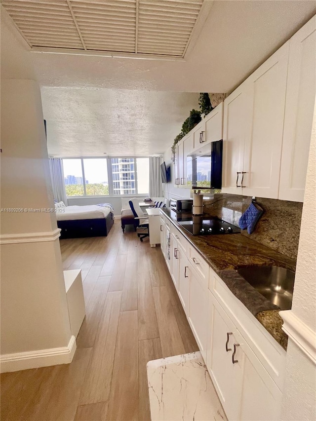 19201 Collins Ave Unit 427, Sunny Isles Beach, FL 33160 - kitchen featuring stainless steel microwave, black electric cooktop, white cabinetry, light wood finished floors, and dark stone counters