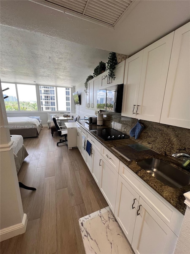 19201 Collins Ave Unit 427, Sunny Isles Beach, FL 33160 - kitchen featuring white cabinetry, wood finished floors, dark stone counters, open floor plan, and black electric cooktop