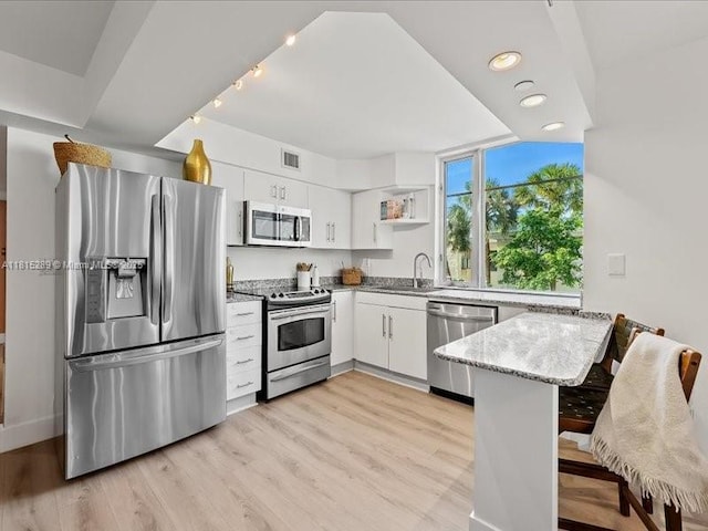 1532 Drexel Ave Unit 204, Miami Beach, FL 33139 - kitchen with appliances with stainless steel finishes, a peninsula, light stone countertops, open shelves, and white cabinets