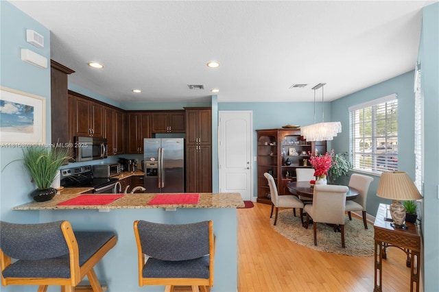 7702 Paddock Pl, Davie, FL 33328 - kitchen featuring stainless steel appliances, a peninsula, light wood finished floors, dark brown cabinetry, and hanging light fixtures