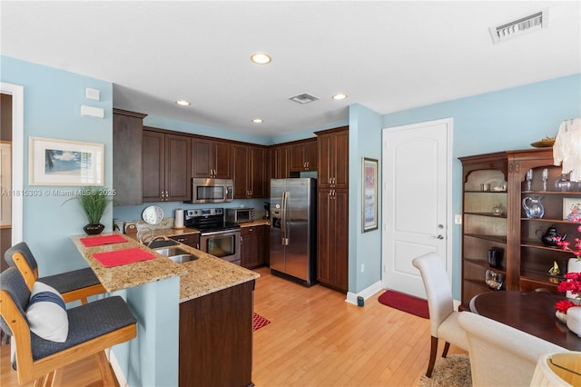 7702 Paddock Pl, Davie, FL 33328 - kitchen featuring appliances with stainless steel finishes, a breakfast bar, light wood finished floors, dark brown cabinets, and recessed lighting