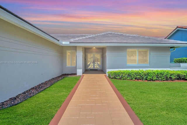 1240 NW 161st Ave, Pembroke Pines, FL 33028 - exterior entry at dusk with french doors, a yard, stucco siding, and a tile roof
