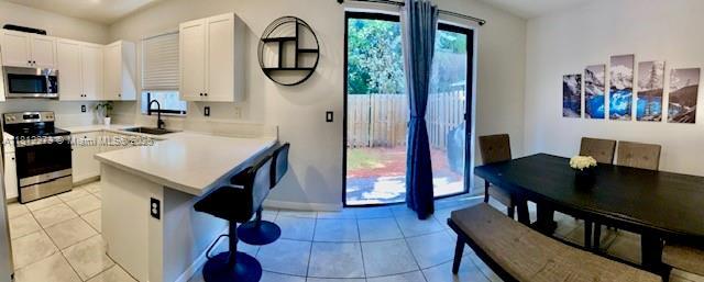 6489 N Anise Ct, Davie, FL 33314 - kitchen with stainless steel appliances, a peninsula, white cabinetry, a breakfast bar, and light tile patterned flooring