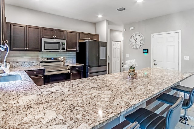 724 SE 37th Ave, Homestead, FL 33033 - kitchen with stainless steel appliances, dark brown cabinets, light stone countertops, backsplash, and a breakfast bar area
