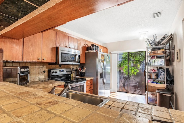 10630 NW 14th St Unit 115, Plantation, FL 33322 - kitchen with stainless steel appliances, a sink, tile counters, backsplash, and brown cabinetry