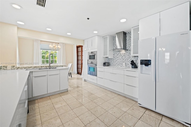 2124 Fisher Island Dr Unit 2124, Miami Beach, FL 33109 - kitchen featuring white fridge with ice dispenser, wall chimney range hood, decorative backsplash, white cabinets, and a chandelier