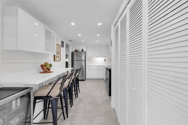 3301 S Palm Aire Dr Unit 106, Pompano Beach, FL 33069 - kitchen featuring freestanding refrigerator, white cabinetry, a peninsula, a kitchen bar, and light tile patterned floors