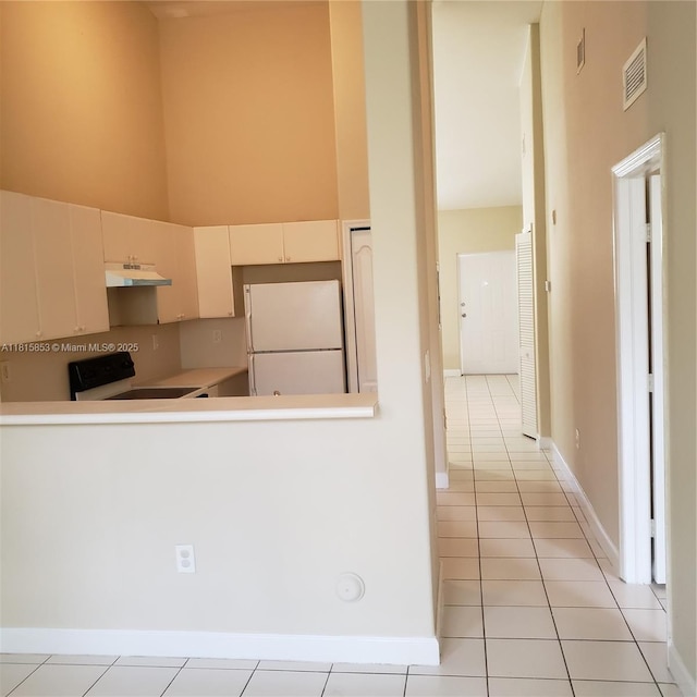 1666 SE 27th Ct Unit 205, Homestead, FL 33035 - kitchen with freestanding refrigerator, stove, light tile patterned floors, under cabinet range hood, and a towering ceiling