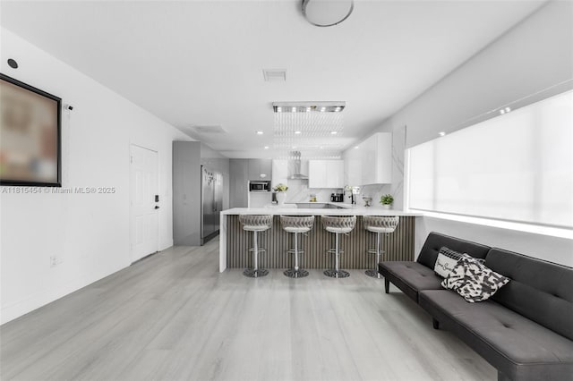 22618 SW 94th Path, Cutler Bay, FL 33190 - kitchen featuring wall chimney exhaust hood, light wood-style floors, a peninsula, light countertops, and a kitchen bar
