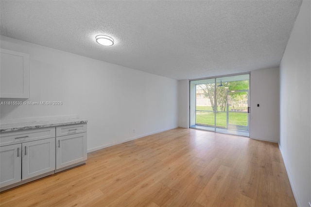 9601 Sunrise Lakes Blvd Unit 106, Sunrise, FL 33322 - empty room featuring a textured ceiling, light wood-style flooring, a wall of windows, and baseboards