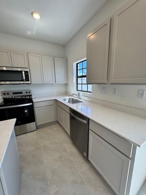 605 NW 6th Ter, Florida City, FL 33034 - kitchen featuring stainless steel appliances, a sink, light tile patterned floors, light stone countertops, and gray cabinets
