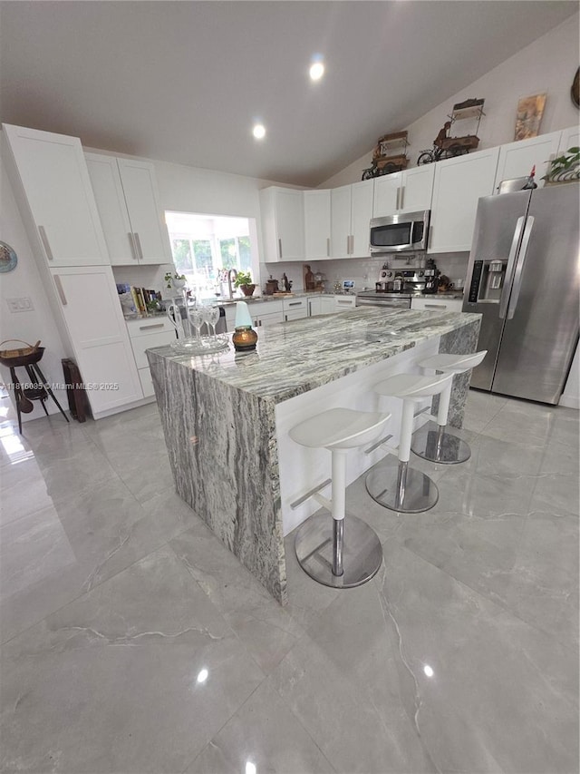 117 SW Fairview Ave, Port St Lucie, FL 34983 - kitchen featuring stainless steel appliances, light stone counters, a large island, lofted ceiling, and white cabinets