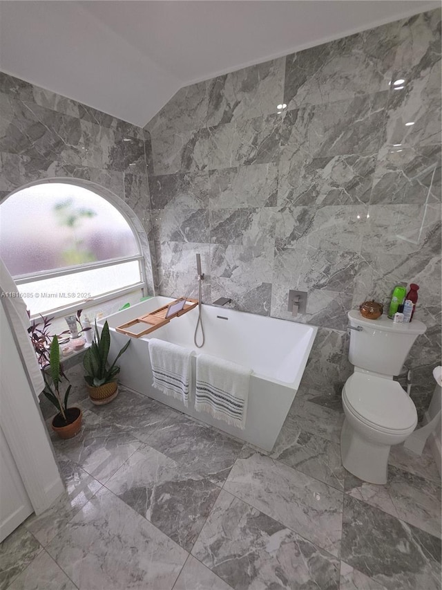 117 SW Fairview Ave, Port St Lucie, FL 34983 - full bath featuring tile walls, a freestanding bath, toilet, marble finish flooring, and vaulted ceiling