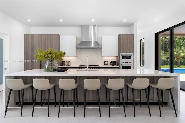 6200 Moss Ranch Rd, Pinecrest, FL 33156 - kitchen featuring wall chimney exhaust hood, modern cabinets, tasteful backsplash, a large island with sink, and white cabinets