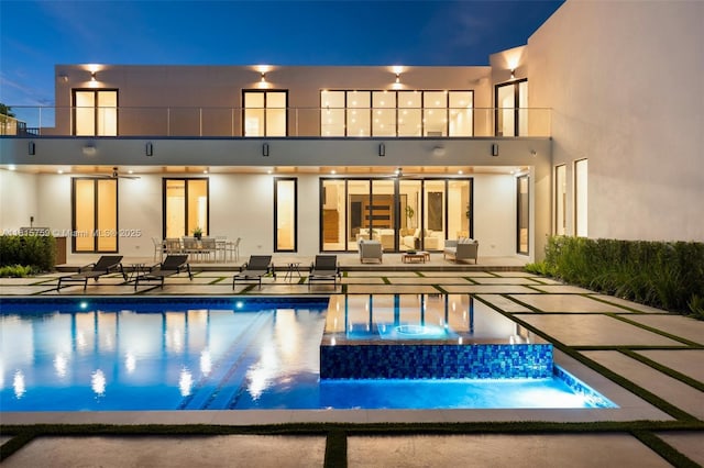6200 Moss Ranch Rd, Pinecrest, FL 33156 - back of house at twilight with a balcony, a patio, a pool with connected hot tub, stucco siding, and an outdoor living space