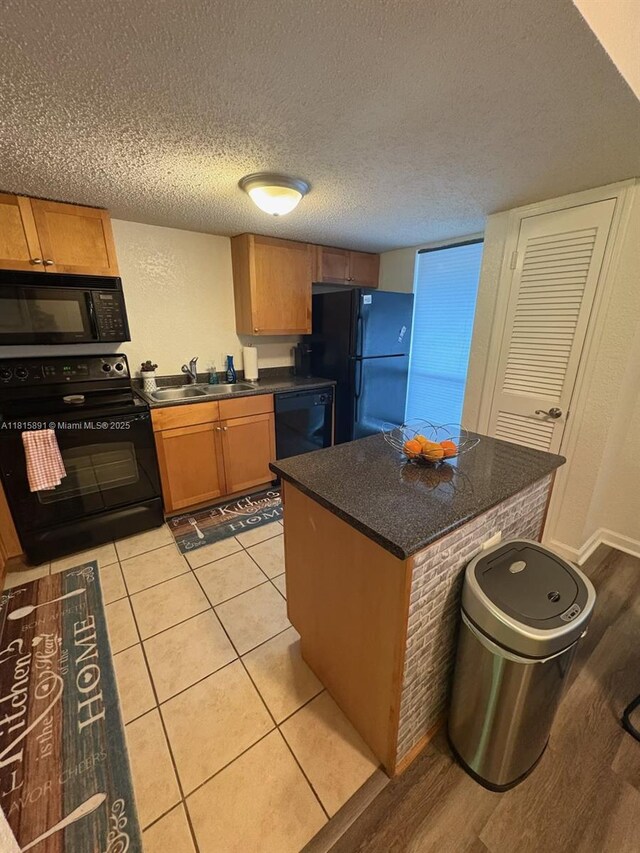 1810 NW 23rd Blvd Unit 103, Gainesville, FL 32605 - kitchen with black appliances, dark countertops, a textured ceiling, a center island, and brown cabinets