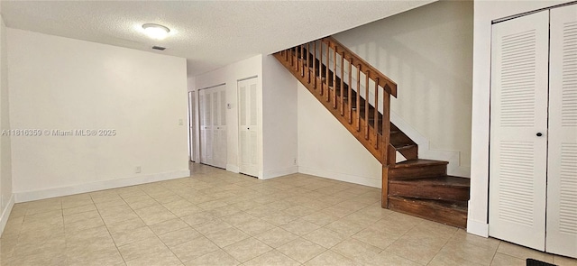 staircase with a textured ceiling, tile patterned flooring, and baseboards