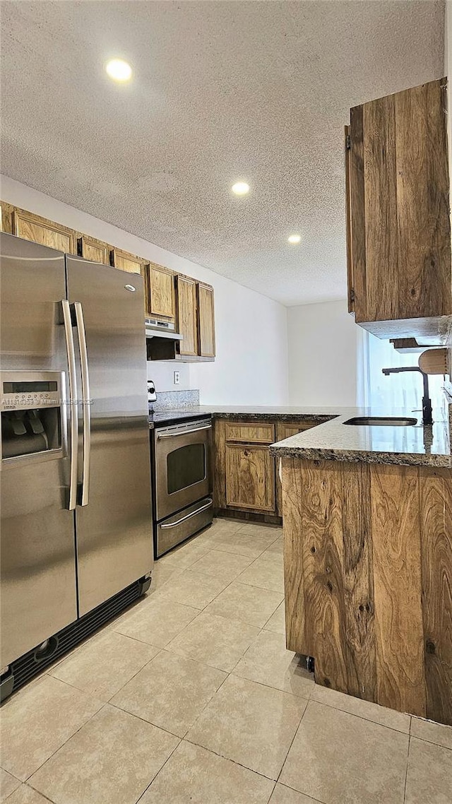 kitchen with appliances with stainless steel finishes, a sink, a textured ceiling, range hood, and brown cabinets