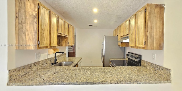 kitchen with a sink, appliances with stainless steel finishes, under cabinet range hood, a textured ceiling, and light stone countertops