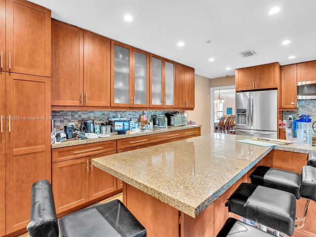 3121 N 52nd Ave, Hollywood, FL 33021 - kitchen featuring appliances with stainless steel finishes, decorative backsplash, brown cabinetry, a kitchen bar, and light stone counters