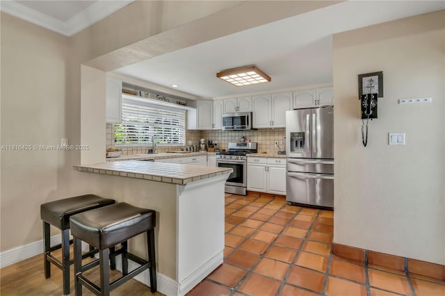 1110 Falcon Ave, Miami Springs, FL 33166 - kitchen with stainless steel appliances, a peninsula, white cabinets, crown molding, and tile countertops