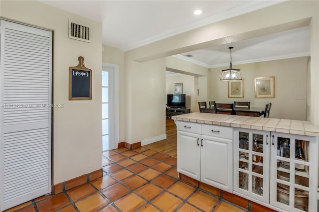 1110 Falcon Ave, Miami Springs, FL 33166 - kitchen featuring tile counters, white cabinets, ornamental molding, baseboards, and hanging light fixtures