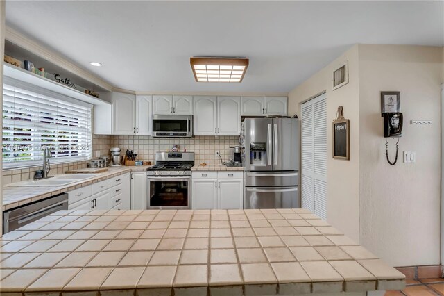 1110 Falcon Ave, Miami Springs, FL 33166 - kitchen featuring stainless steel appliances, tile countertops, a sink, backsplash, and white cabinetry