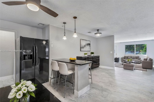 735 NE 38th St, Oakland Park, FL 33334 - kitchen featuring black fridge with ice dispenser, a textured ceiling, a breakfast bar, dark countertops, and light marble finish flooring