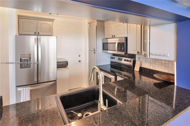 430 Golden Isles Dr Unit 301, Hallandale Beach, FL 33009 - kitchen featuring stainless steel appliances, decorative backsplash, a sink, and dark stone counters